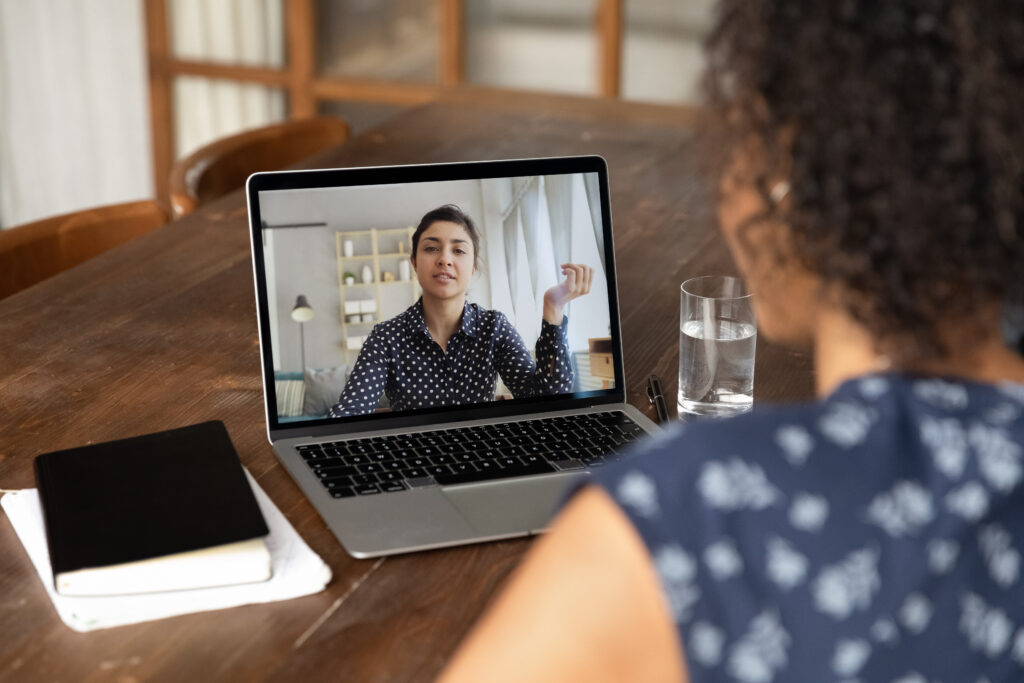 Back view close up African American woman making video call to Indian colleague, using laptop and webcam, diverse workers or friends chatting online, involved in conference, consulting client