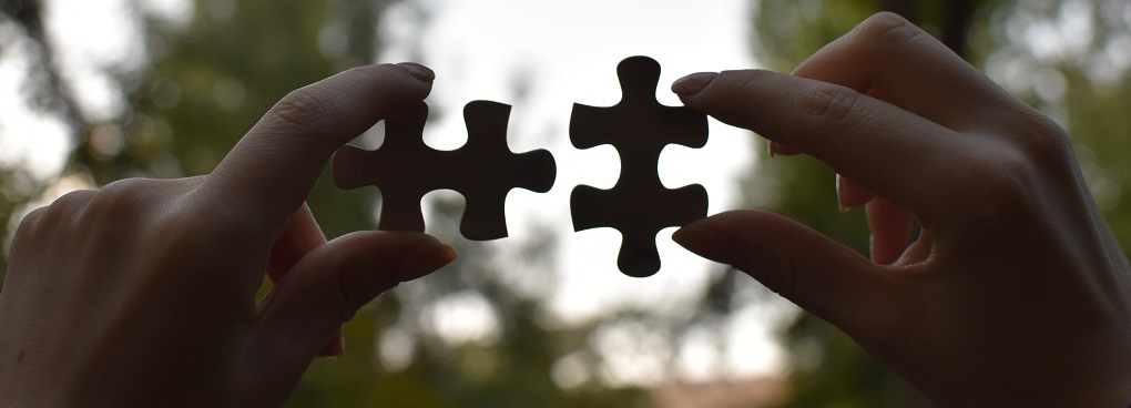 Two hands bringing together two interlocking puzzle pieces.