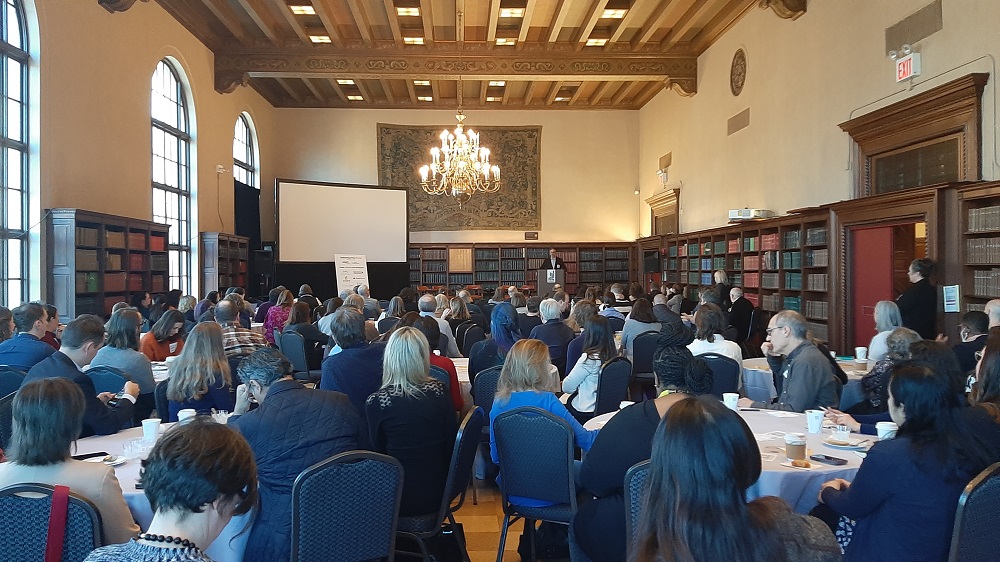 A group of people sitting around tables listening to a speaker in a library.